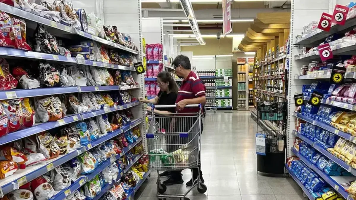 Estanterías vacías de un supermercado porteño junto a una fila de compras en un hipermercado del conurbano