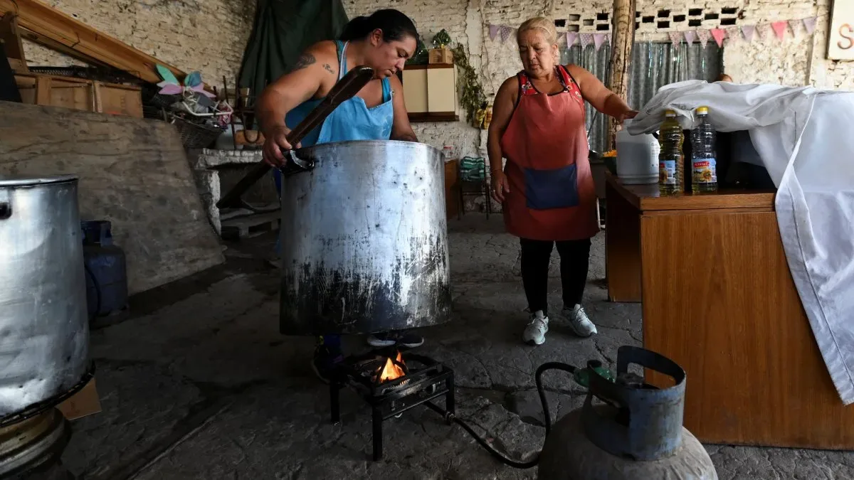 Mujer en barrio popular separando poca comida en platos pequeños sobre mesa humilde