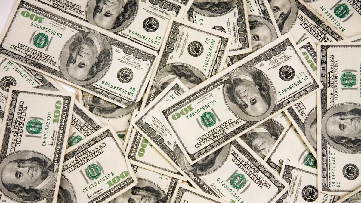 Economista Alberto Ades en una conferencia financiera con gráficos de dólar y mercados de fondo
