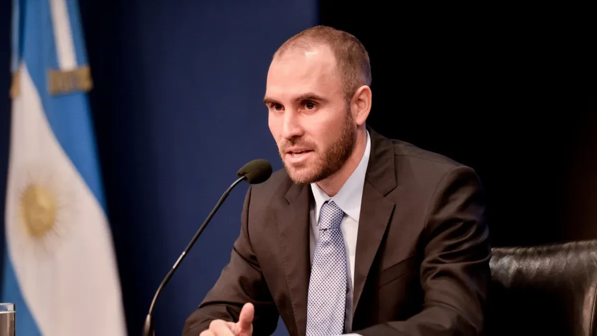 Martín Guzmán hablando en una conferencia con gesto serio y micrófono