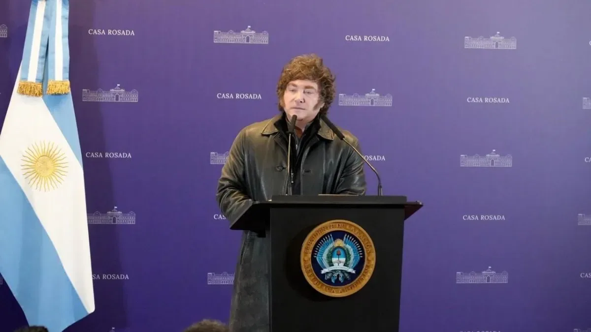 Javier Milei hablando en conferencia de prensa en Casa Rosada con micrófonos y bandera argentina al fondo