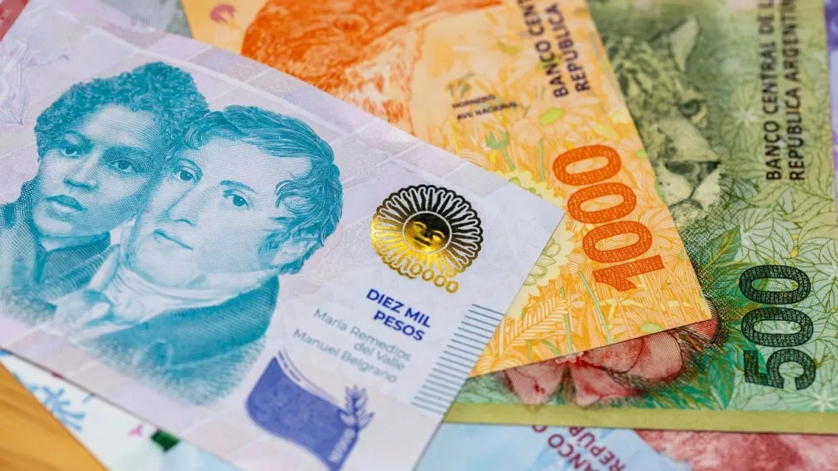 Persona contando billetes de pesos argentinos en una mesa con facturas y una calculadora